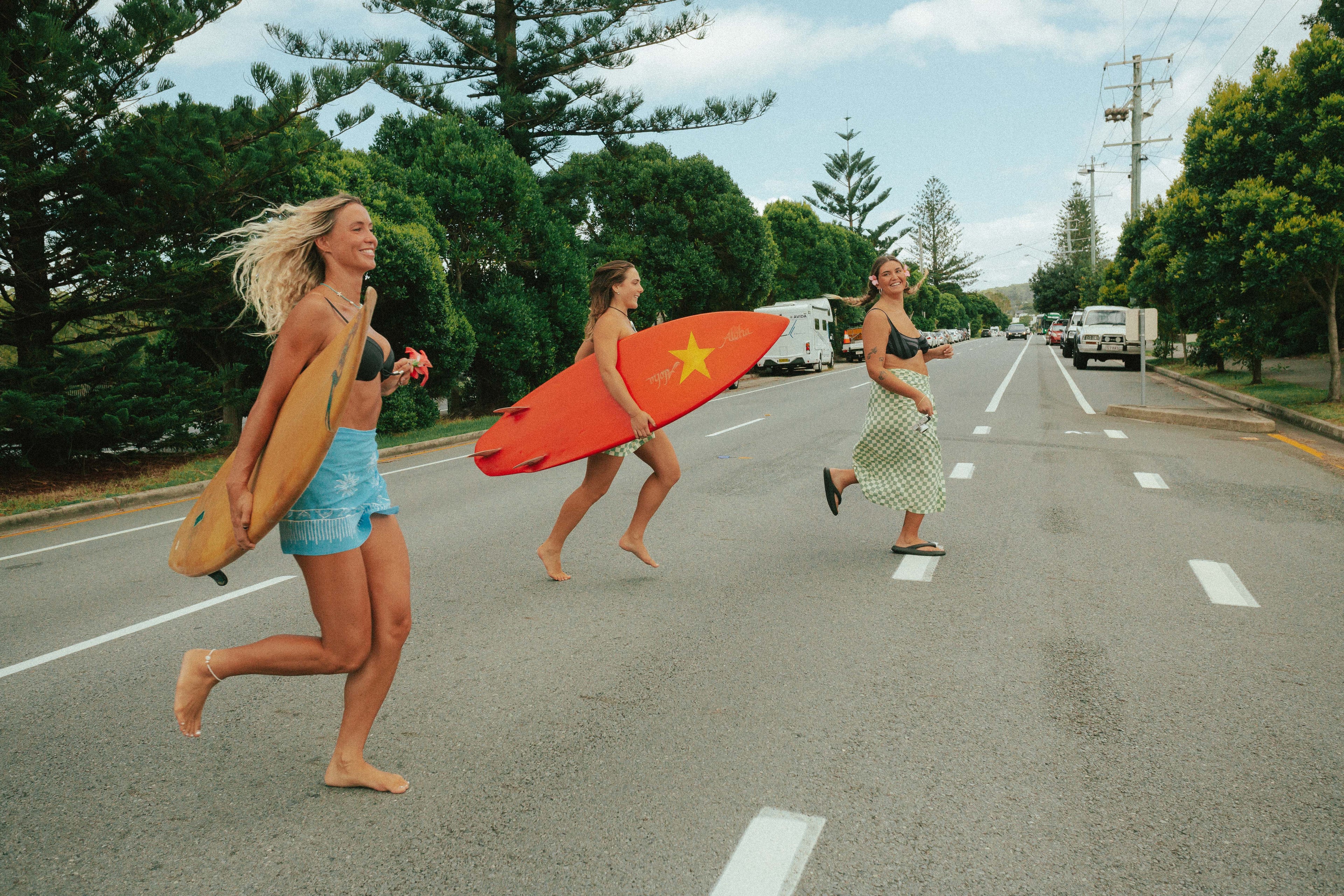This image shows three girls running across the street wearing the Sun Animals sarongs. Two are holding surf boards.
