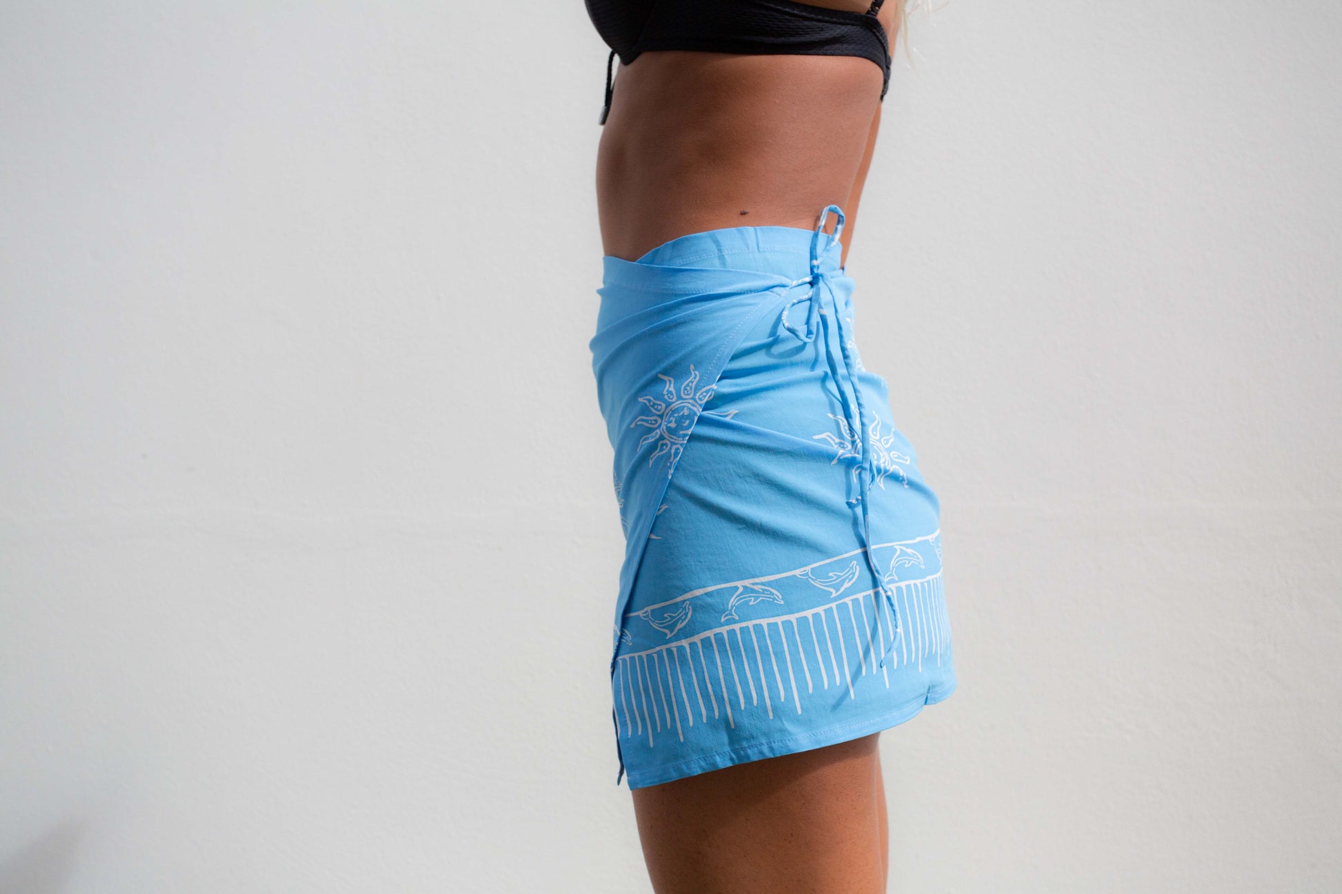 Girl wearing a light blue wrap skirt with a white print of suns and dolphins.