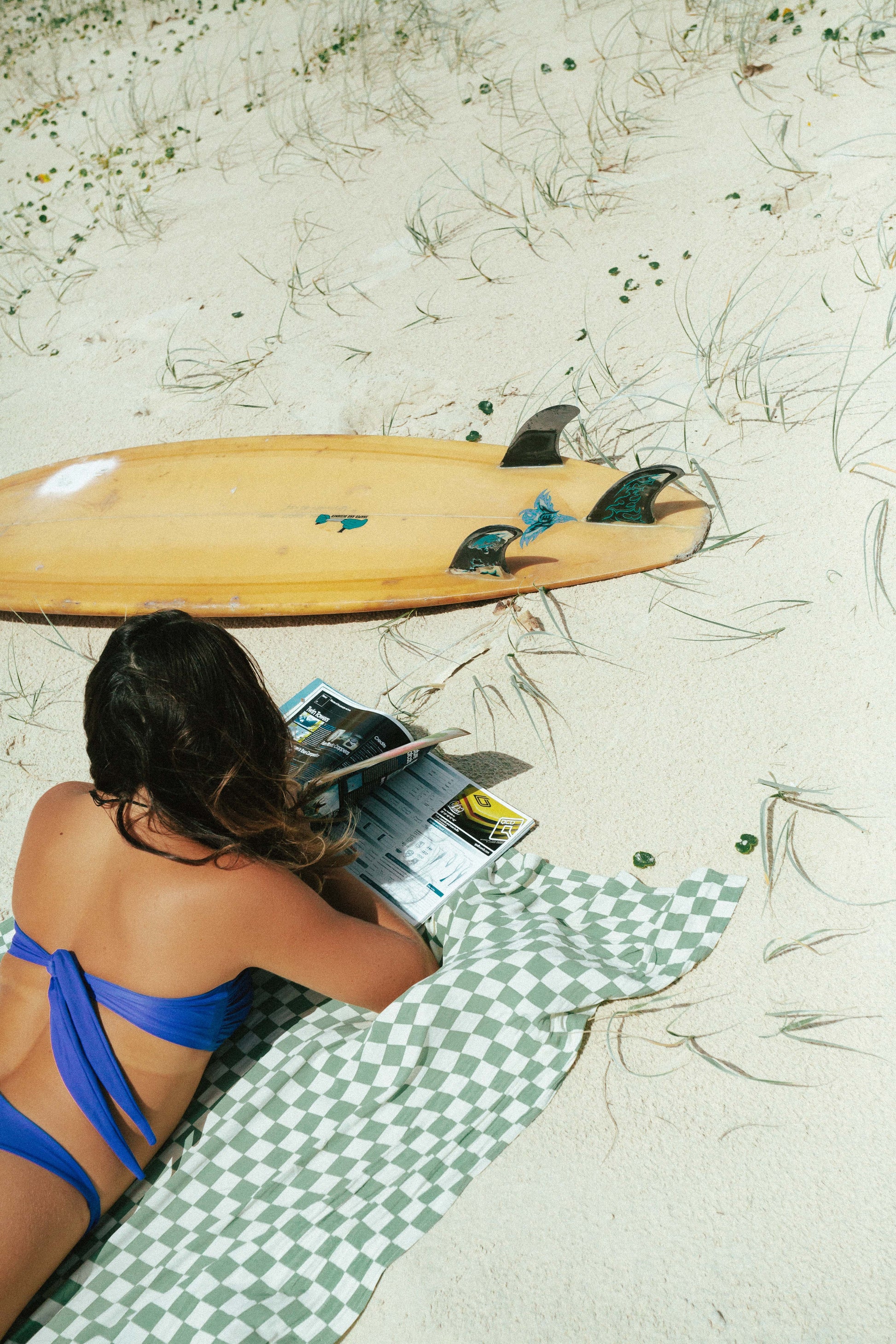 checkered white and green sarong, pictured here with a model reading and a surfboard